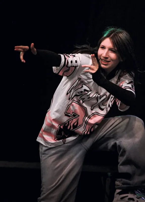 Kas Raines performing on stage in a graphic streetwear tee, striking a dance pose