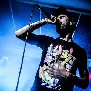 None Like Joshua on stage bathed in blue light, hand on chest, delivering an emotional performance