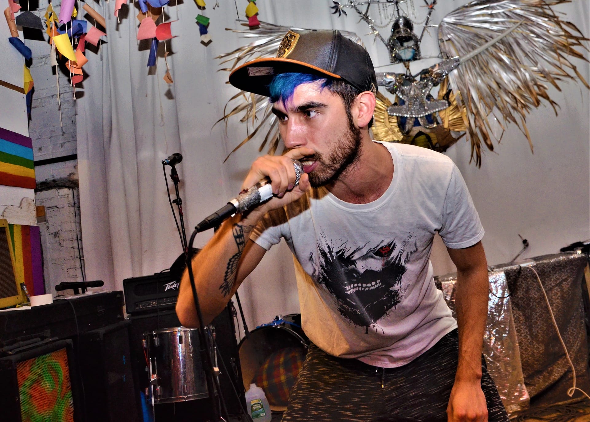 None Like Joshua performing with blue hair and snapback, rapping into mic at an intimate venue show